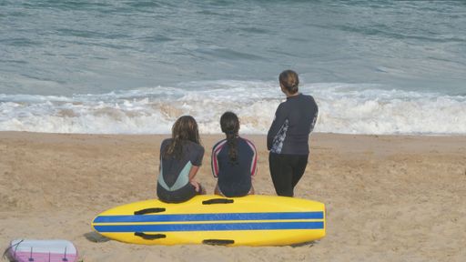 rear view of three women with yellowsurfboard on sand at the beach looking out to water