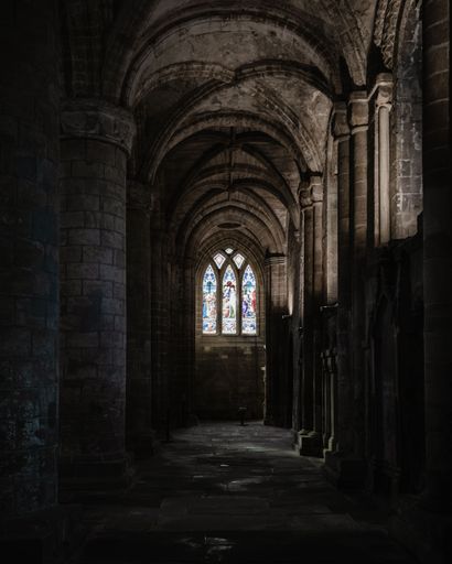The interior of an ancient stone cathedral with pillars, arches, and large windows in Scotland, UK