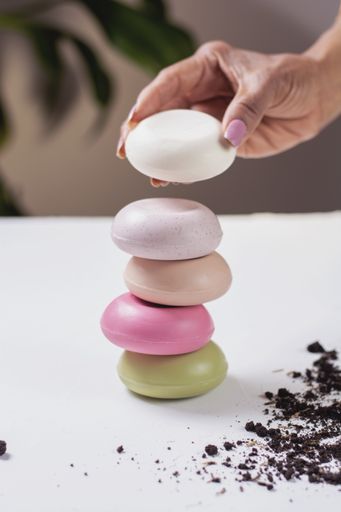 A vertical shot of a female hand taking one of the colorful organic soaps set on top of each other
