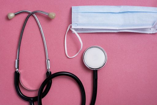 A top view of a stethoscope and face mask on pink background - medical concept