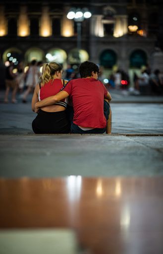 A vertical shot of a loving couple holding each other in the street in Piazza del Duomo, Milan, Italy