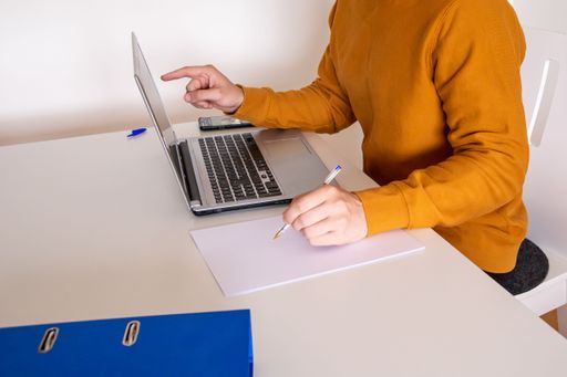 A female taking notes while working with a laptop