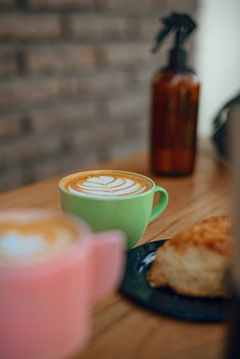 A vertical shot of 2 cups of latte coffee with a leaf pattern on a wooden table
