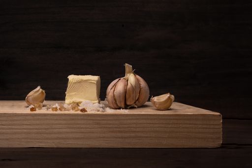 A closeup of garlic cloves and butter on a wooden board under the lights