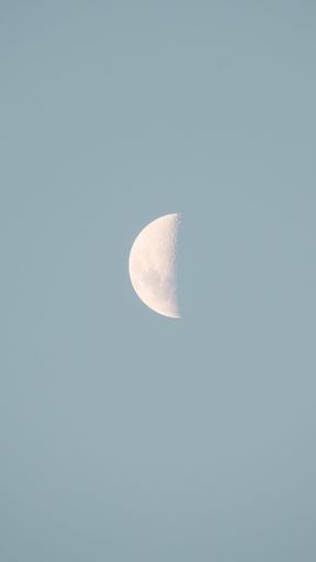A vertical shot of a beautiful half moon in the bright blue sky