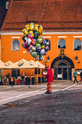 A vertical shot of a person dressed as a clown with cartoon balloons standing in Old Square