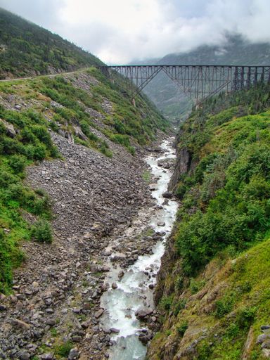 An old bridge over a river flowing through rocks under a blue cloudy sky during the daytime