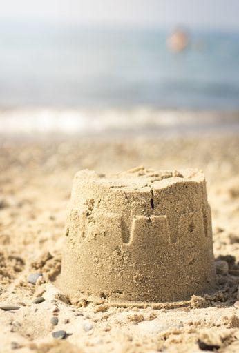 A vertical shot of a small sandcastle at beach under the sunlight with a blurry background