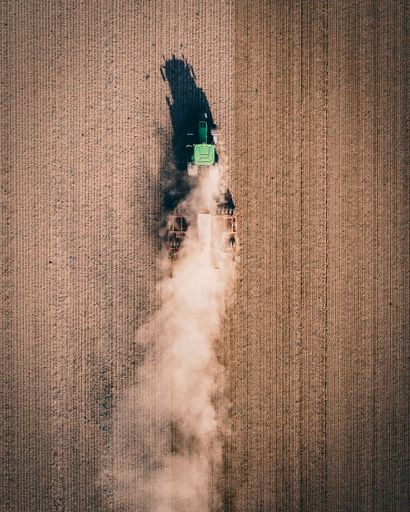 A vertical drone shot of a tractor working in the field and making dust