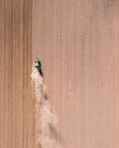 A vertical drone shot of a tractor working in the field and making dust