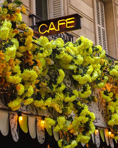 a vertical shot of a cafe entry with nice yellow flowers and a "cafe" neon sign