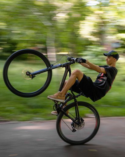 A young man in casual clothing, riding a bicycle, performing a stunt of mid-air flip