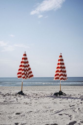 A line of closed umbrellas with red strips standing on a sandy beach in the morning