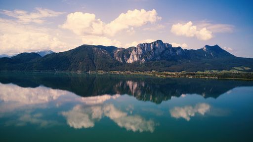 A beautiful view of mountain range and cloudy sky reflecting on a lake in Moondsee, Austria