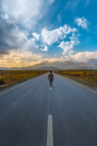 A vertical shot of a man walking on an asphalted countryside road