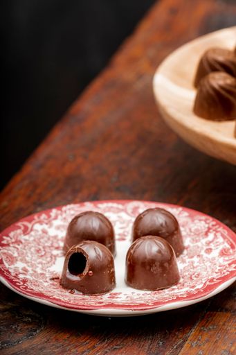 A vertical shot of a plate with four pieces of chocolate and one is bitten