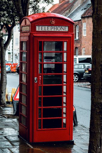 A vertical shot of a red telephone booth after rain on a street in London