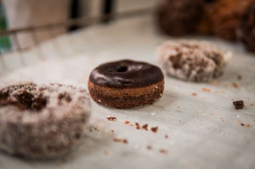 A chocolate glazed donut in selective focus with other donuts blurred in the background