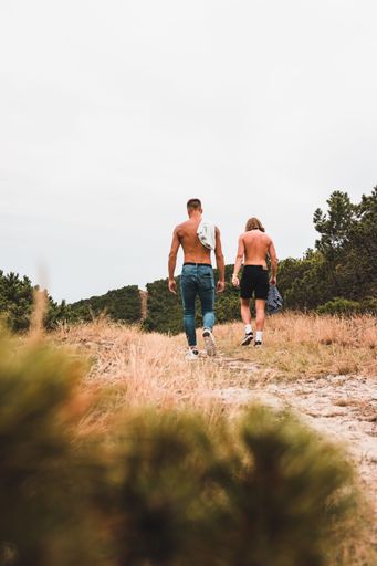 A vertical shot of two half-naked males walking in a field surrounded by trees