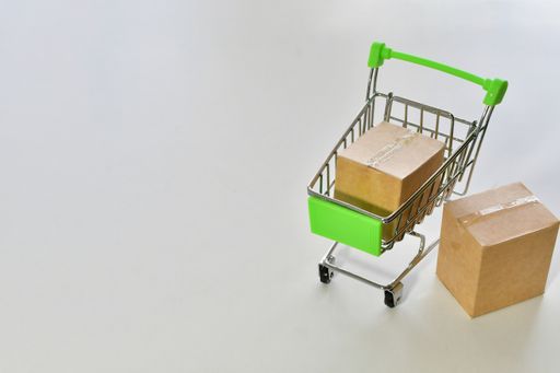 A high angle shot of small cartons on a miniature shopping cart on a white surface