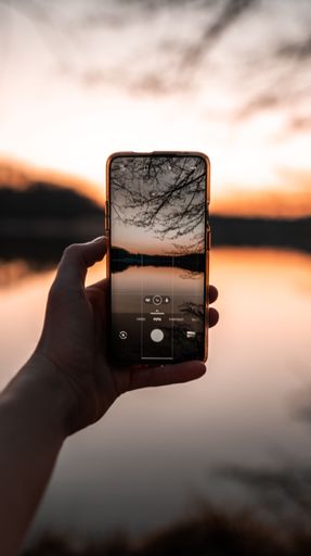A person taking photo of a calm lake during sunset using a smartphone