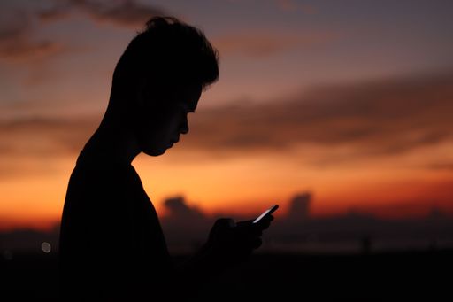 A silhouette of a man holding a phone on a background of sunset