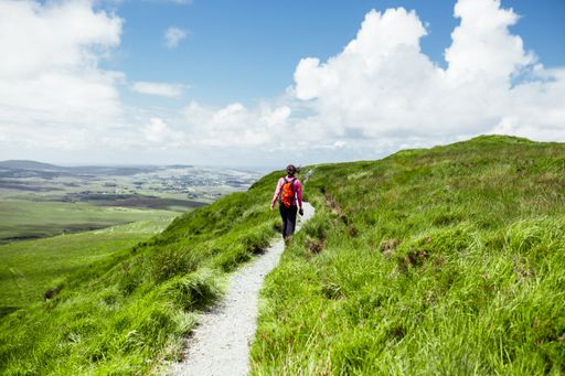 A beautiful shot of a female hiker with an orange backpack walking through a path in the hills