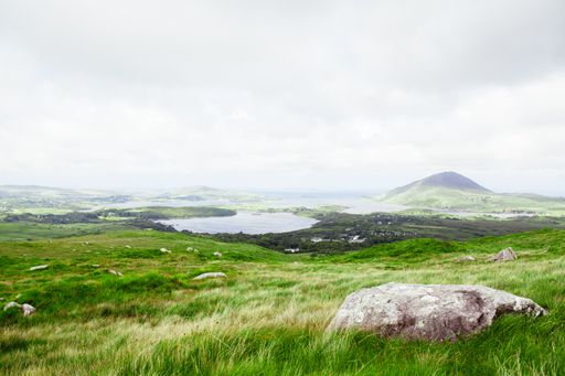 A beautiful shot of a big stone in a green valley with the cloudy sky in the background