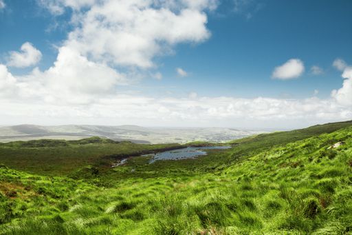A beautiful shot of a green valley and a small lake in it with the bright cloudy sky in the background