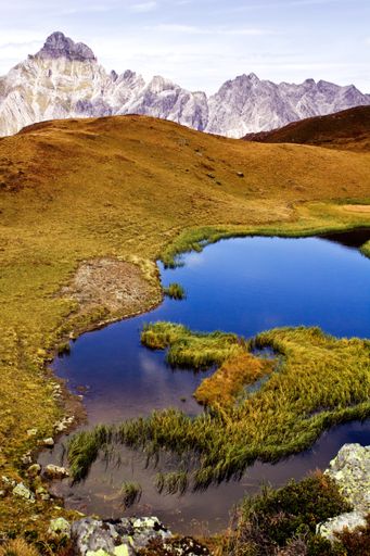 A vertical shot of a bright blue lake in a yellow valley and rocks in the background