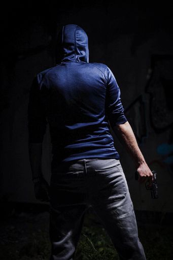 A vertical of a hooded man seen from behind, holding a gun