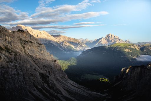 The Italian Dolomites in the early morning at sunrise, hugged by mist and clouds. Rolling green hills and sheer white cliffs, blue skies