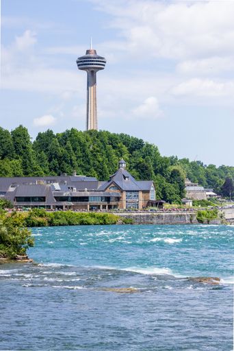 A beautiful view of the Niagra Falls with the forest trees and Skylon Tower under cloudy sky, Canada