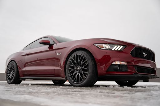 A low angle shot of red luxury Ford Mustang 5.0 parked on icy road