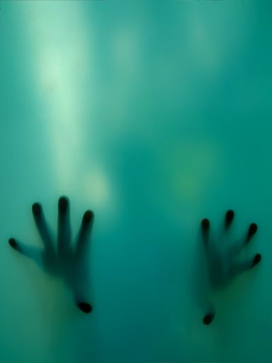 A vertical shot of scary hands of a woman from the back of a green glass portrait