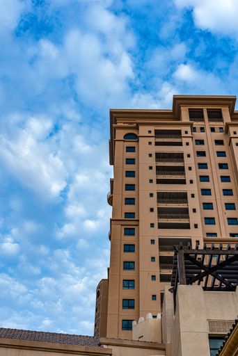 A vertical low angle shot of brown modern urban building against blue cloudy sky