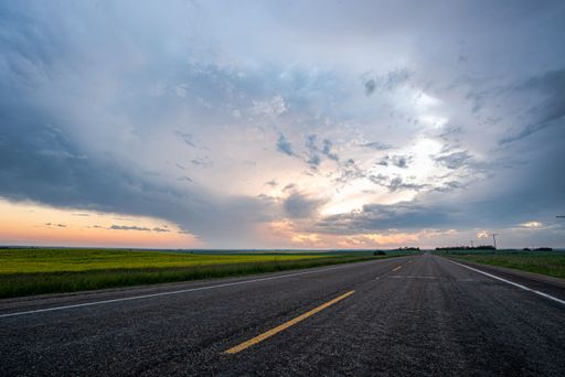 A beautiful display of a stormy sky captured along an asphalt road with yellow marking lines at sunset