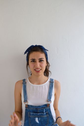 A vertical shot of a beautiful Hispanic brunette girl in blue overalls looking at the camera with a confused expression