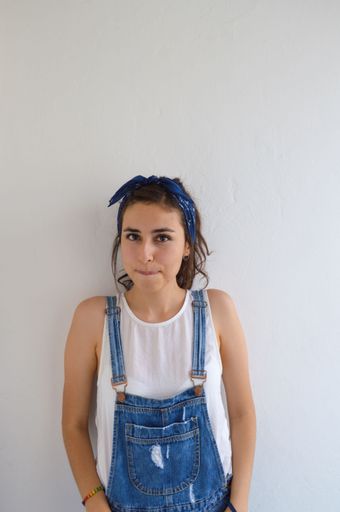 A vertical shot of a confident brunette girl with a cute blue bandana and overalls looking at the camera