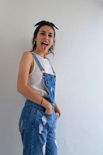 A vertical shot of a self-confident girl in blue overalls being silly and sticking her tongue out at the camera