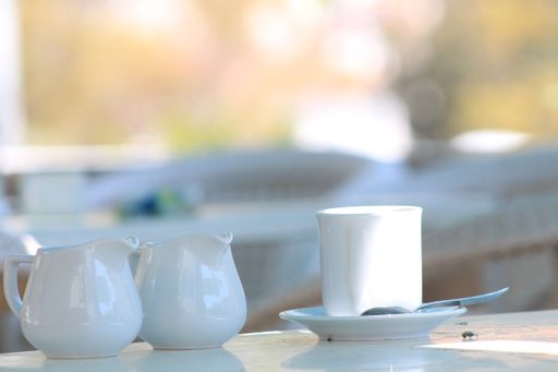 A closeup shot of a white coffee cup and two tiny cute white teapots next to it on blurred background
