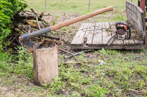 An axe stuck in a log captured during wood cutting and a chainsaw next to it