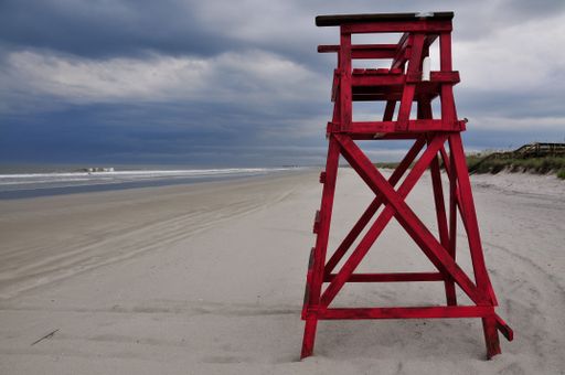 An abandoned lifeguard station with calm ocean waves and a cloudy sky in the background