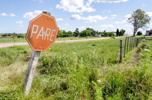 A stop traffic sign in a field with trees and fences