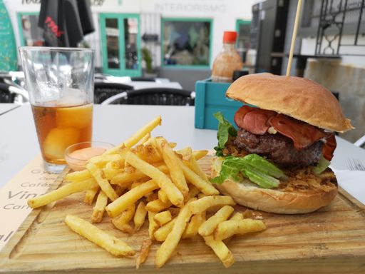 A closeup of a delicious beef burger with french fries on a wooden board with ice tea