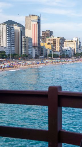 A vertical shot of high buildings on the beach with a wooden fence on the foreground in Rio de Janeiro