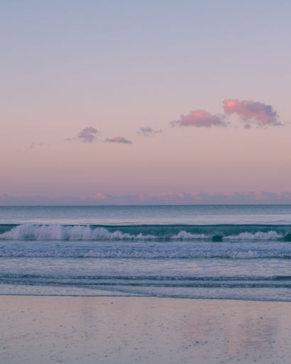A vertical shot of a beautiful beach and the horizon with a few clouds in the morning sky