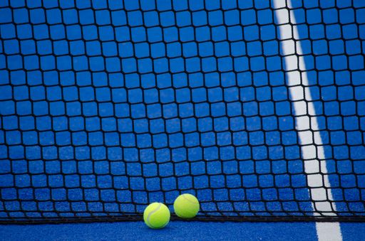 Blue paddle tennis court, two balls next to the net, racket sports concept
