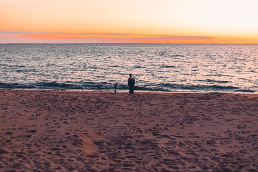 A man standing on the sand of the beach looking to the sunset over the ocean