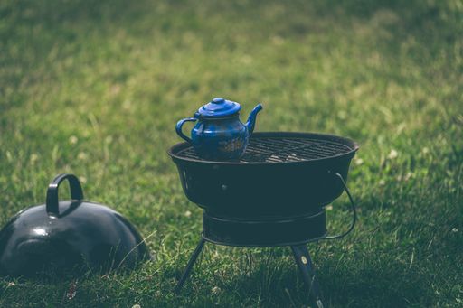 A closeup of a blue teapot on a grill weber isolated on the green grass